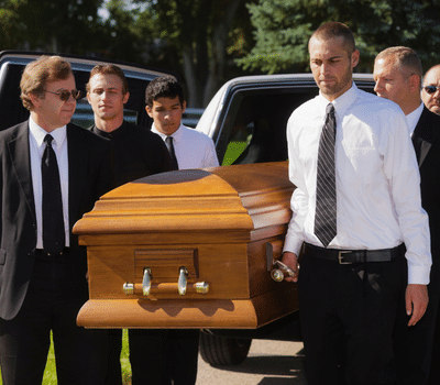 Men wearing traditional black and white funeral attire carrying a wooden coffin