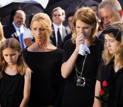 Women and girls of different ages wearing traditional black funeral attire, gathered outdoors with mourners during a funeral service